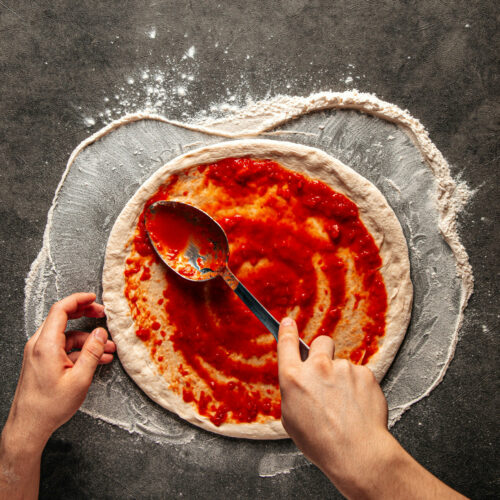 Person spreading sauce on pizza