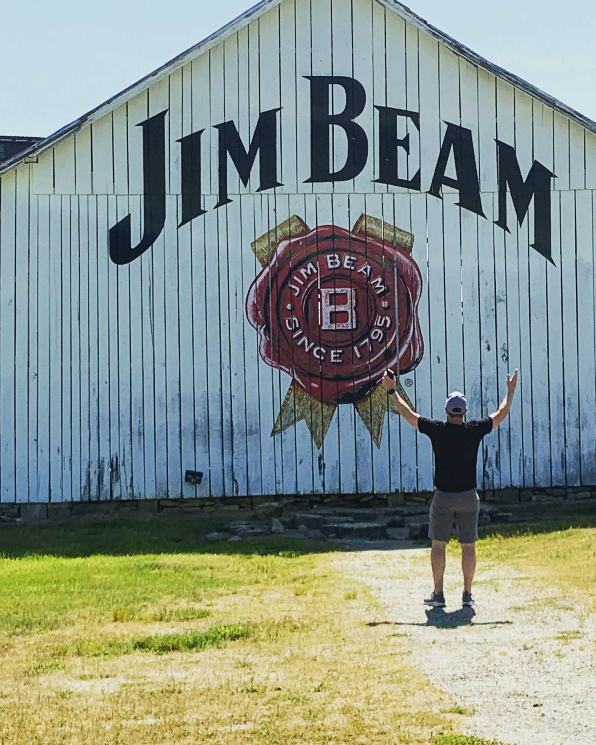 Man poses in front of white barn with Jim Beam logo