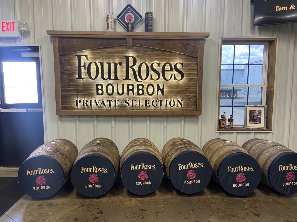 Six barrels of Four Roses Bourbon sit against a wall with a Four Roses sign