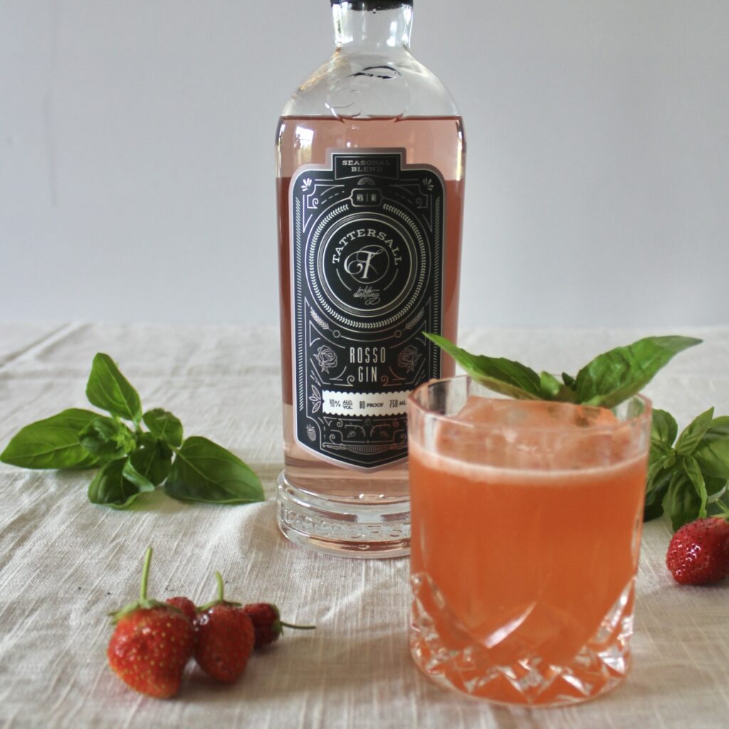 Pink cocktail, garnished with basil, sits in front of a bottle of Tattersall Rosso Gin.