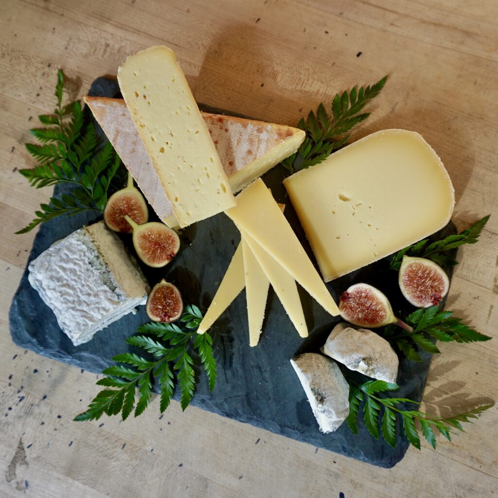 American Artisan Cheeses on a black board, garnished with ferns and figs