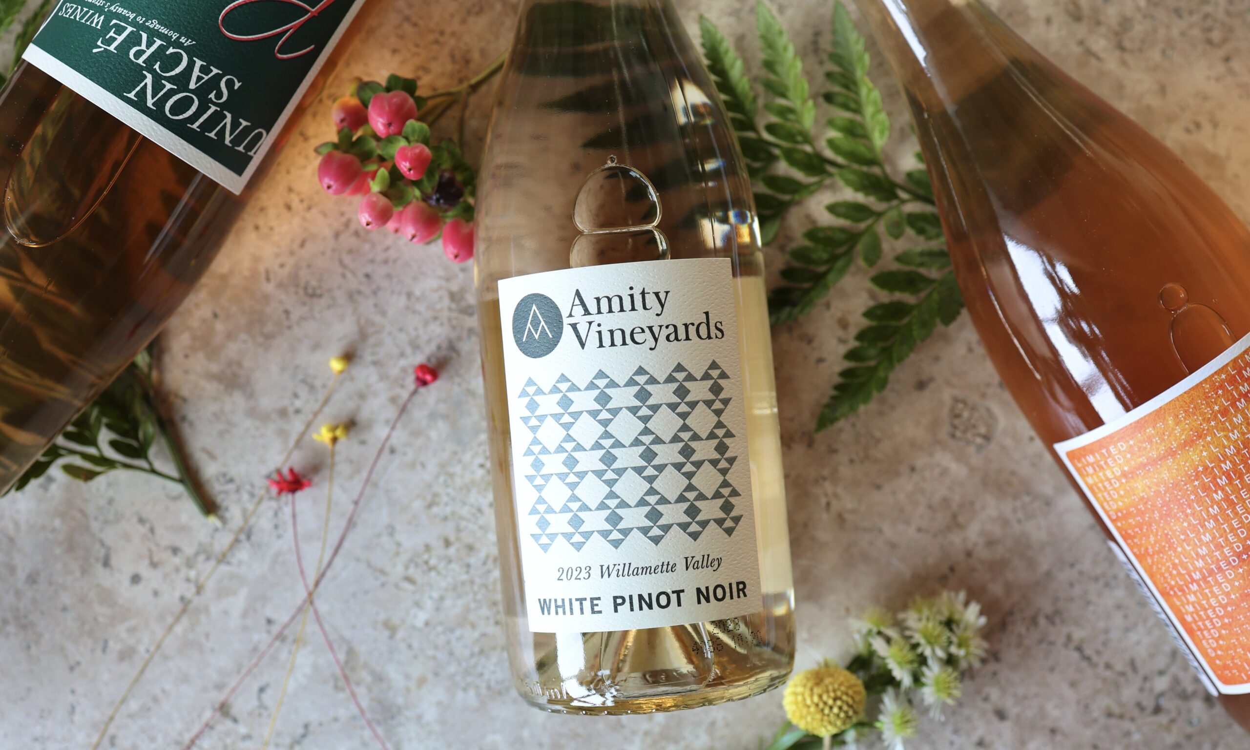 3 bottles of wine on a table with greenery and flowers