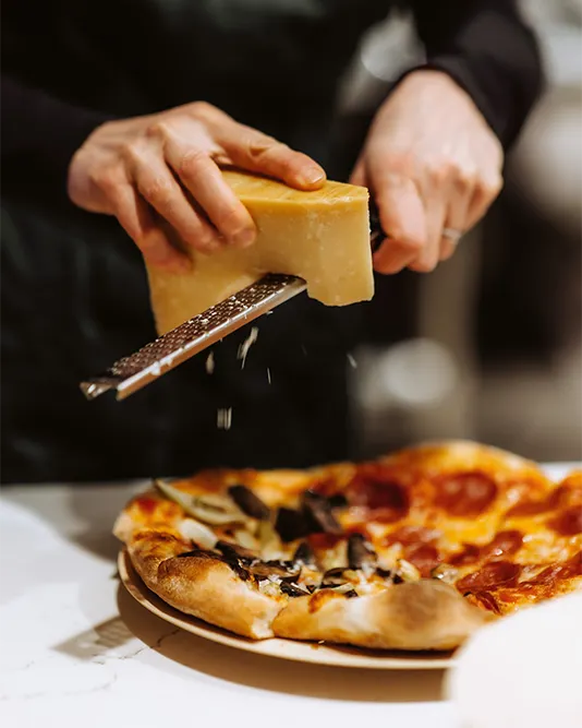 hands shredding parmesan over pizza