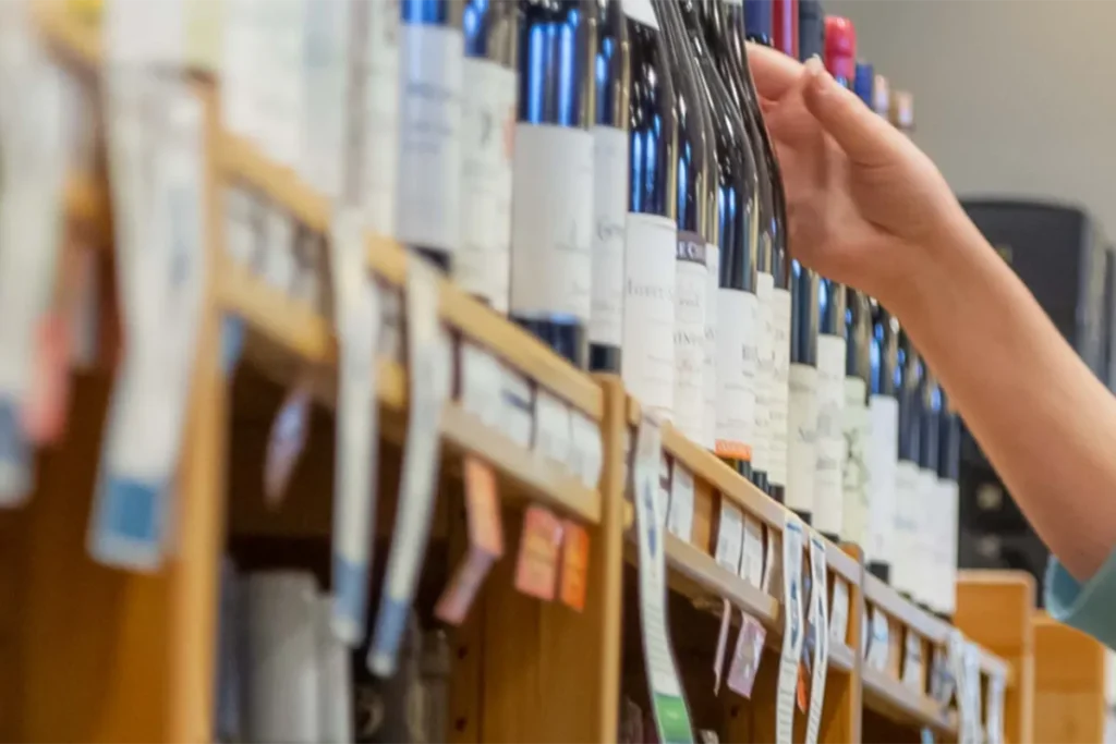 hand reaching for bottle of wine on shelf