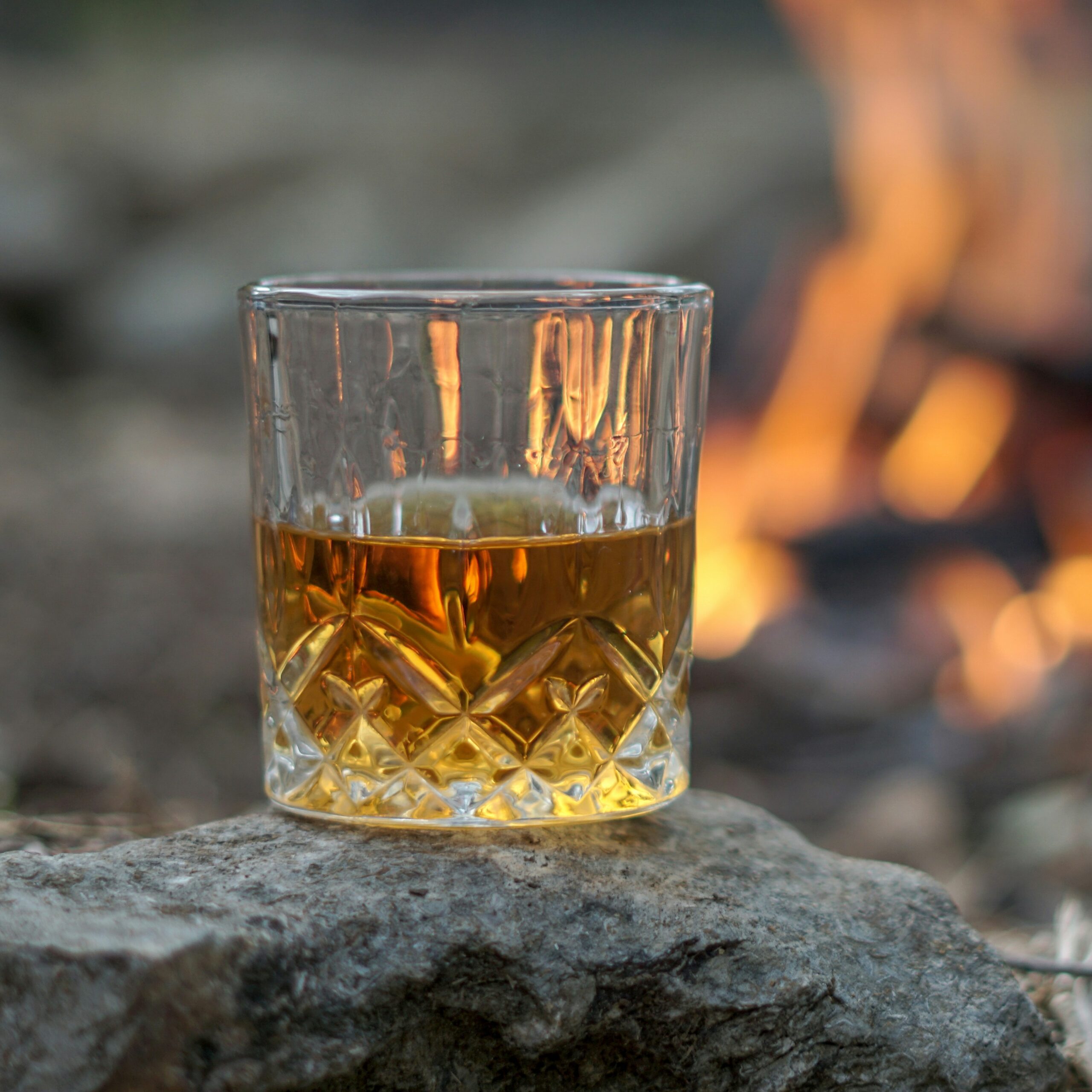 glass of bourbon sitting on a rock by a fire