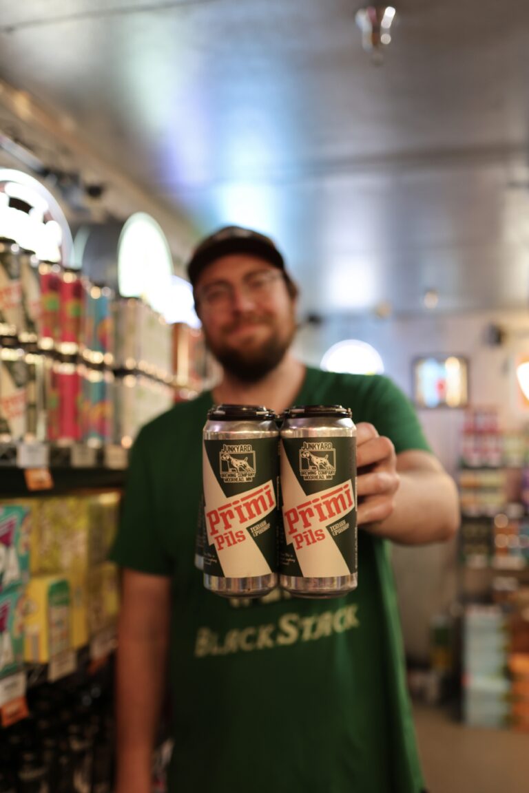 Stephen holding up a 4 pack of Primi Pilsner