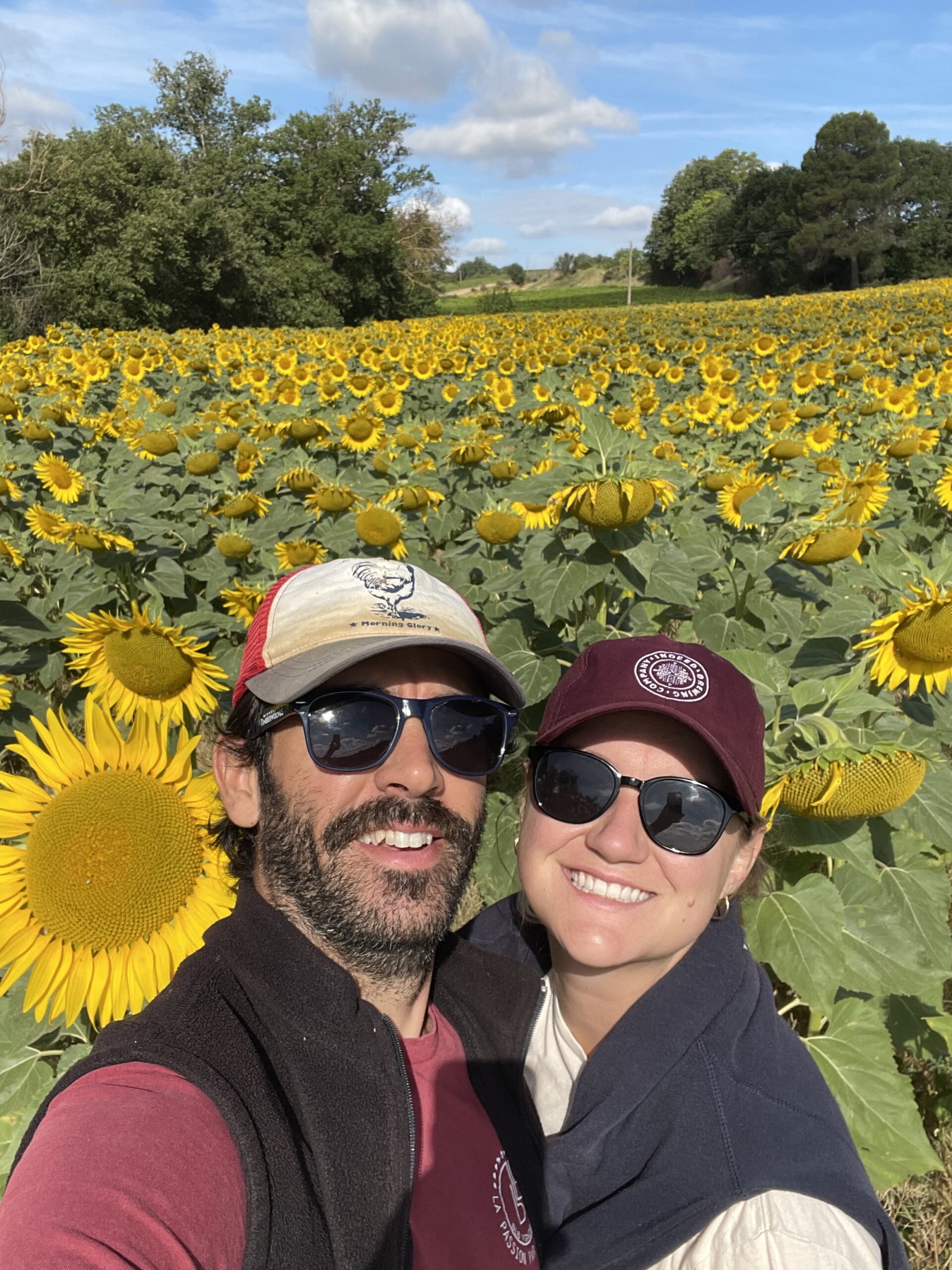 Claire smiling in a field of sunflowers with her husband, Morgan