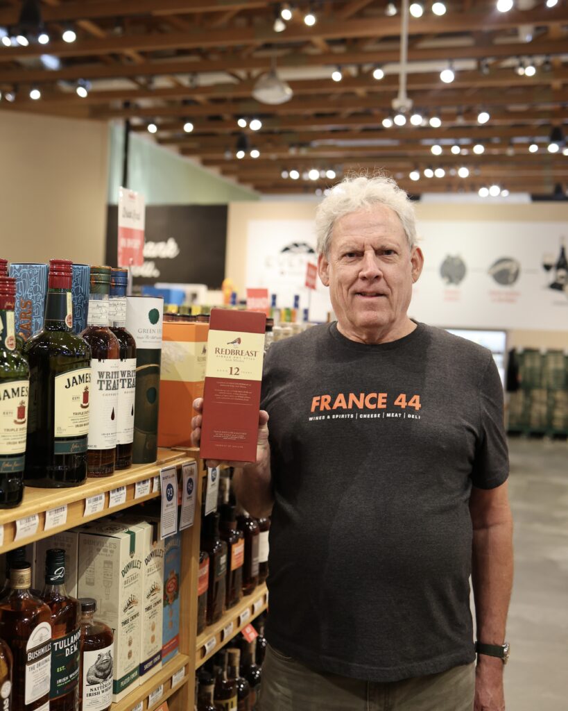 Jim holding up a box of Redbreast 12-year Irish Whiskey in the Whiskey aisle of France 44