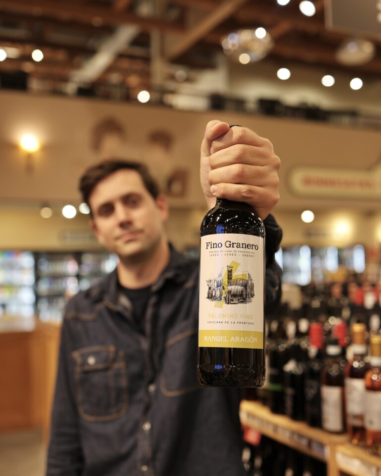 Austin holds out a bottle of sherry in the fortified wine aisle