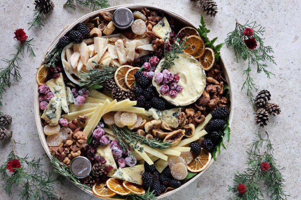 holiday cheese board surrounded with greenery & pinecones