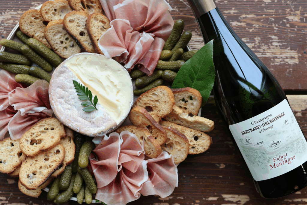 Rush Creek surrounded by cornichons, speck and crostini, beside a bottle of bubbles