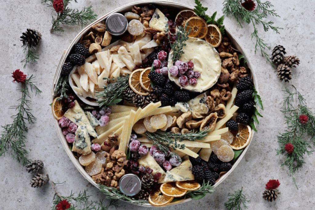 holiday cheese board surrounded with greenery & pinecones