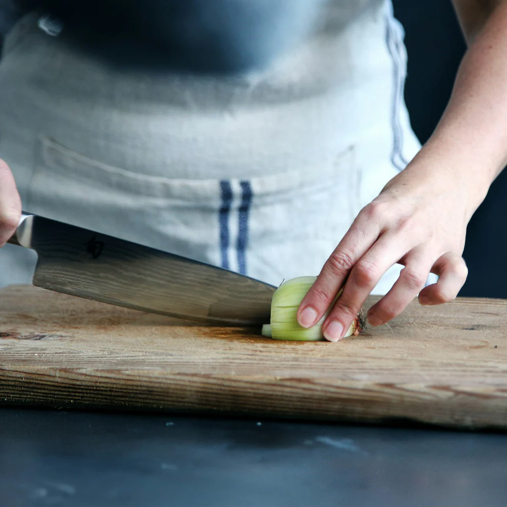 Person in apron cutting a cucumber on a wooden cutting board