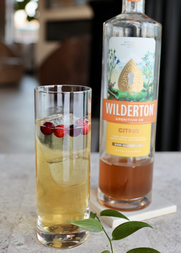 Highball with light orange cocktail beside a bottle of Wilderton N/A Cirtus Aperetivo
