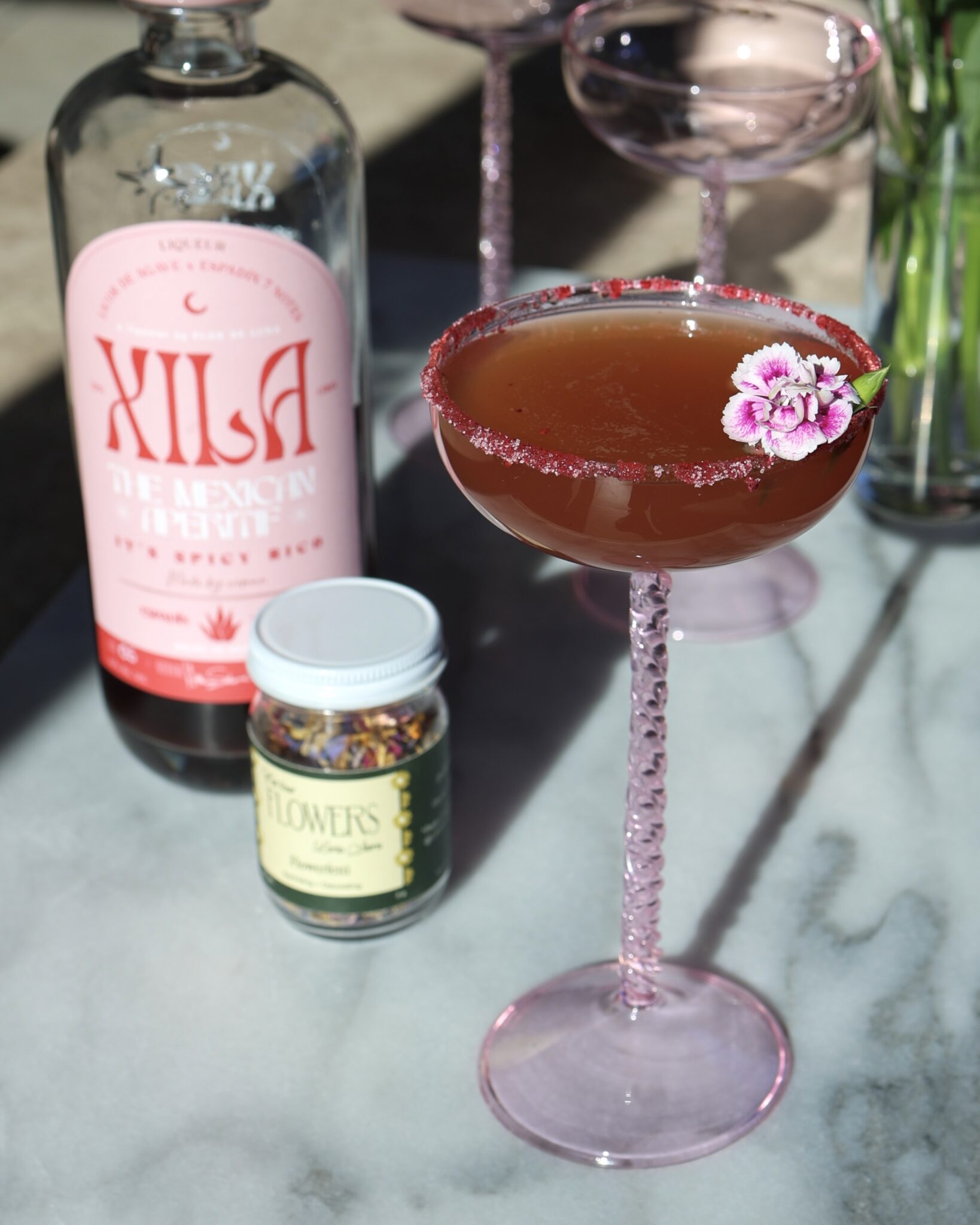 red cocktail in a pink coupe garnished with flowers