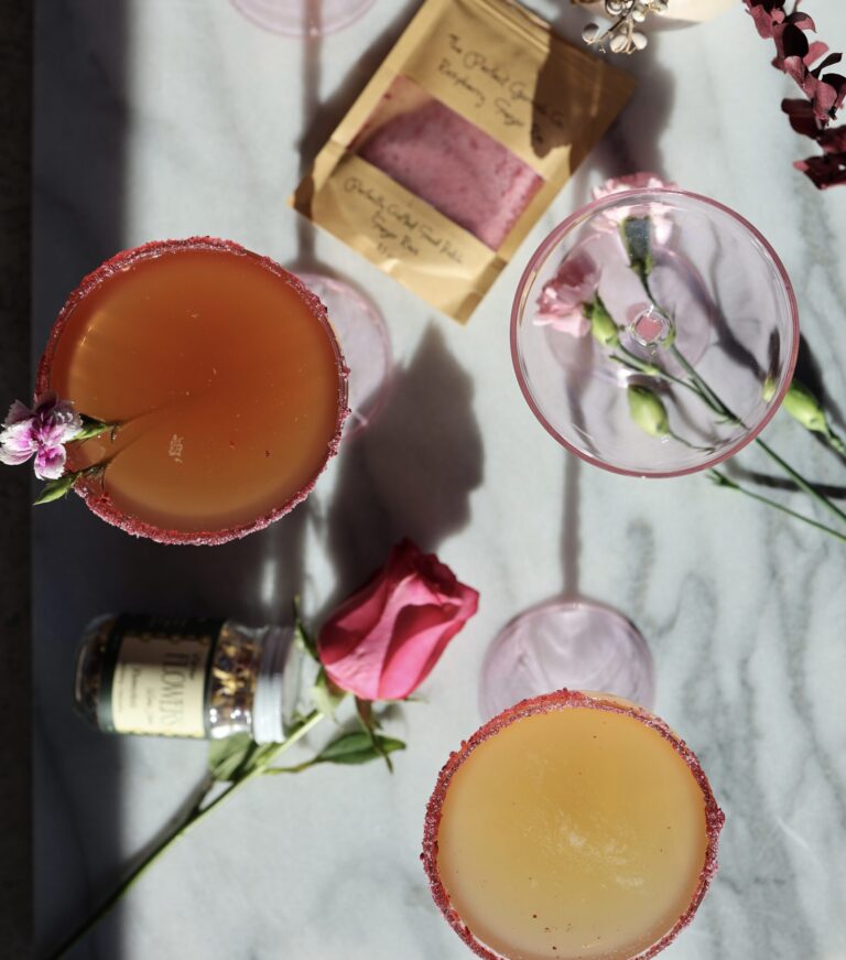 two cocktails on a marble table with a rose and raspberry sugr