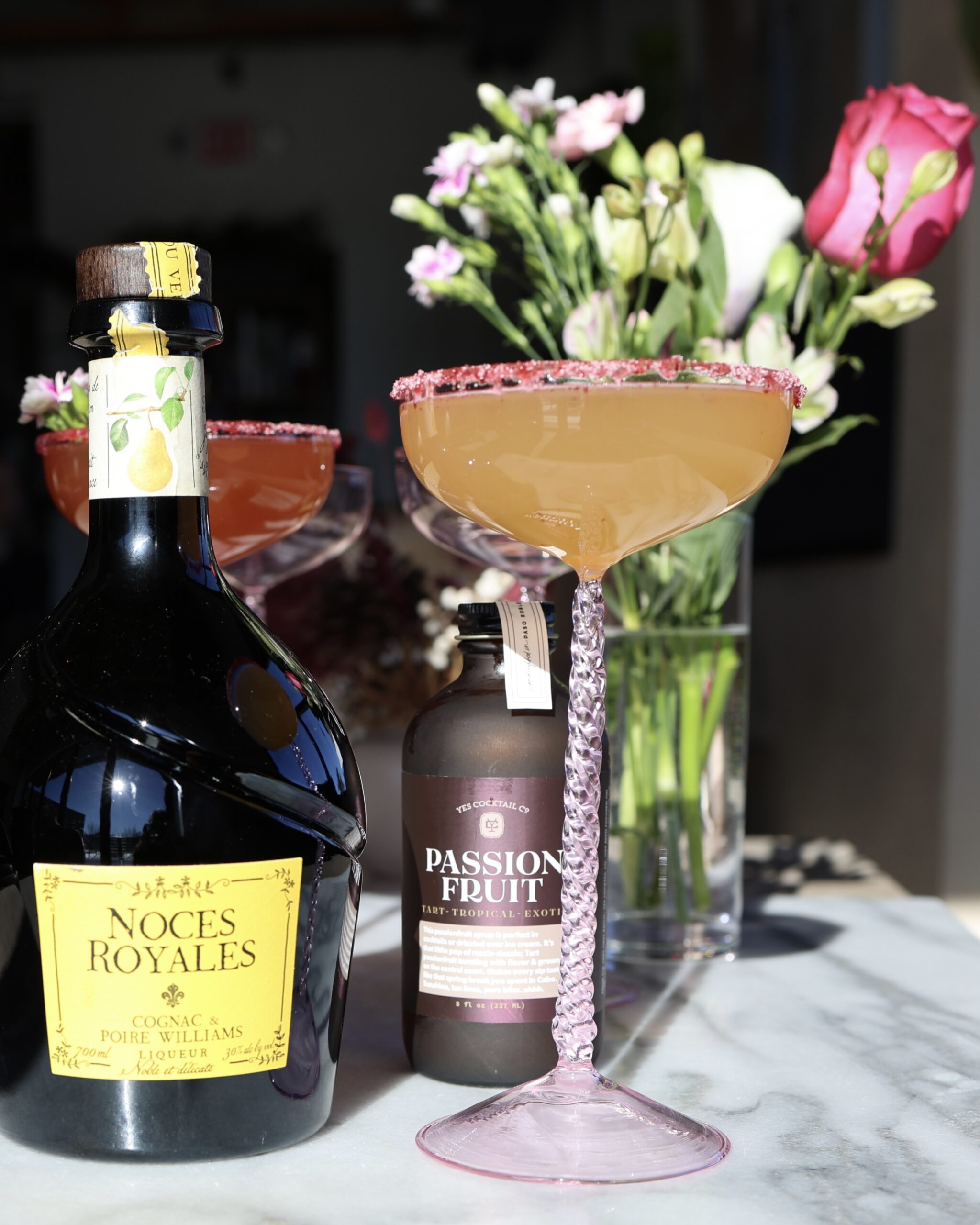 orange cocktail in a pink coupe garnished with a pink sugar rim