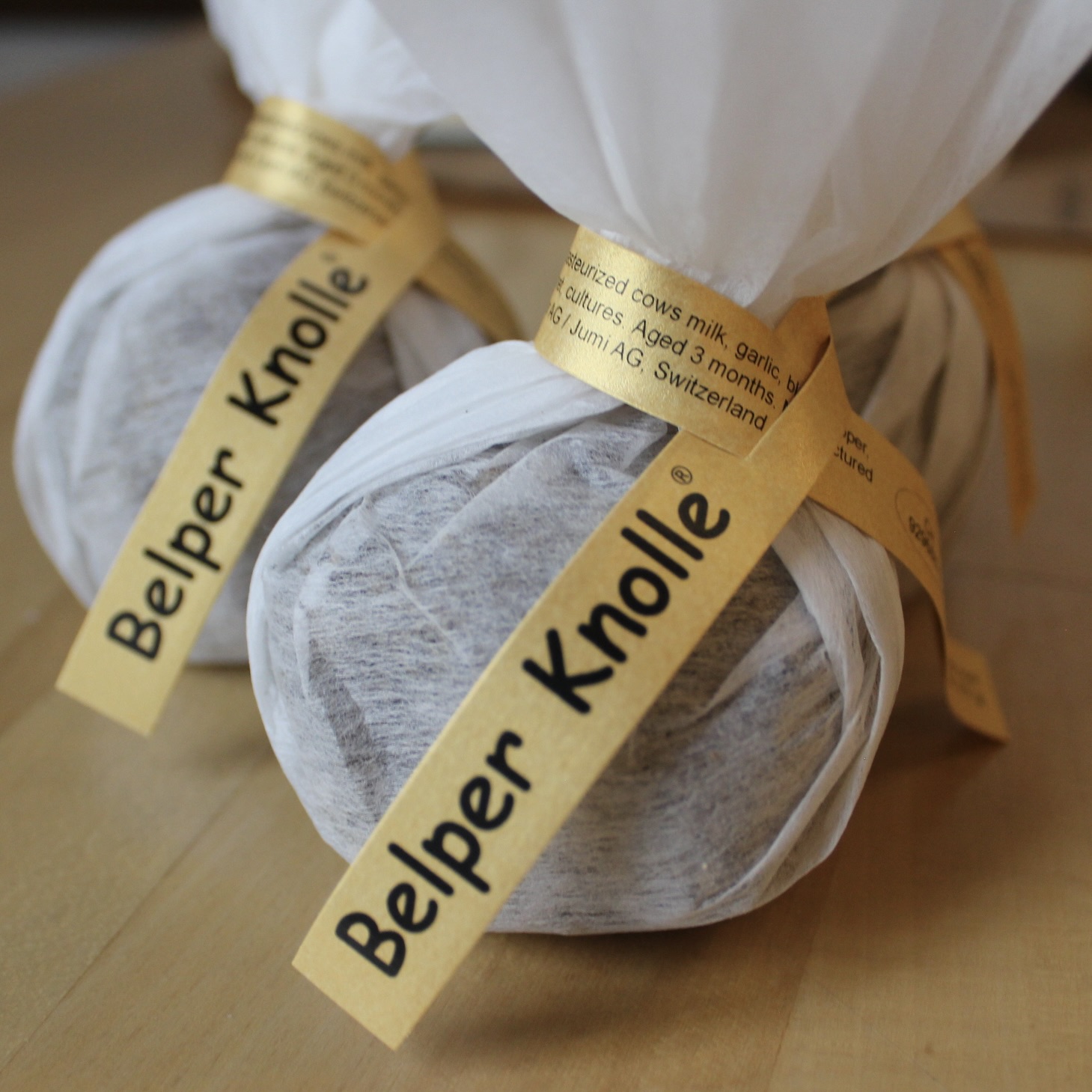 Two little cheeses wrapped in white cloth with yellow tags reading "Belper Knolle"