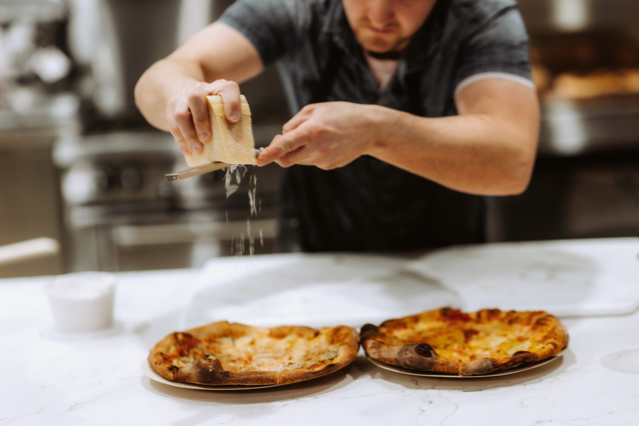 grating parmigiano regigano on a pizza