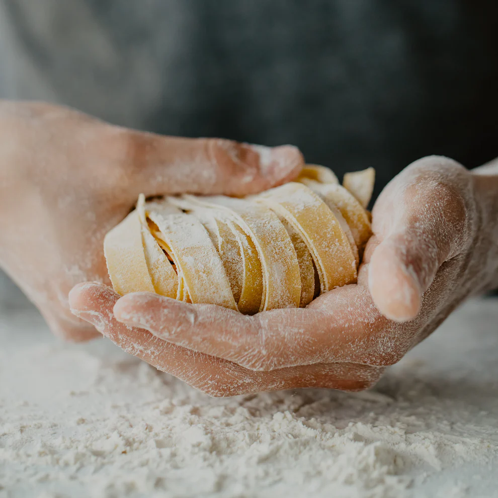 Two hands holding a bunch of fresh linguini over a floury surface