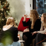 3 people sit in the lounge with glasses of wine gazing at a Christmas tree