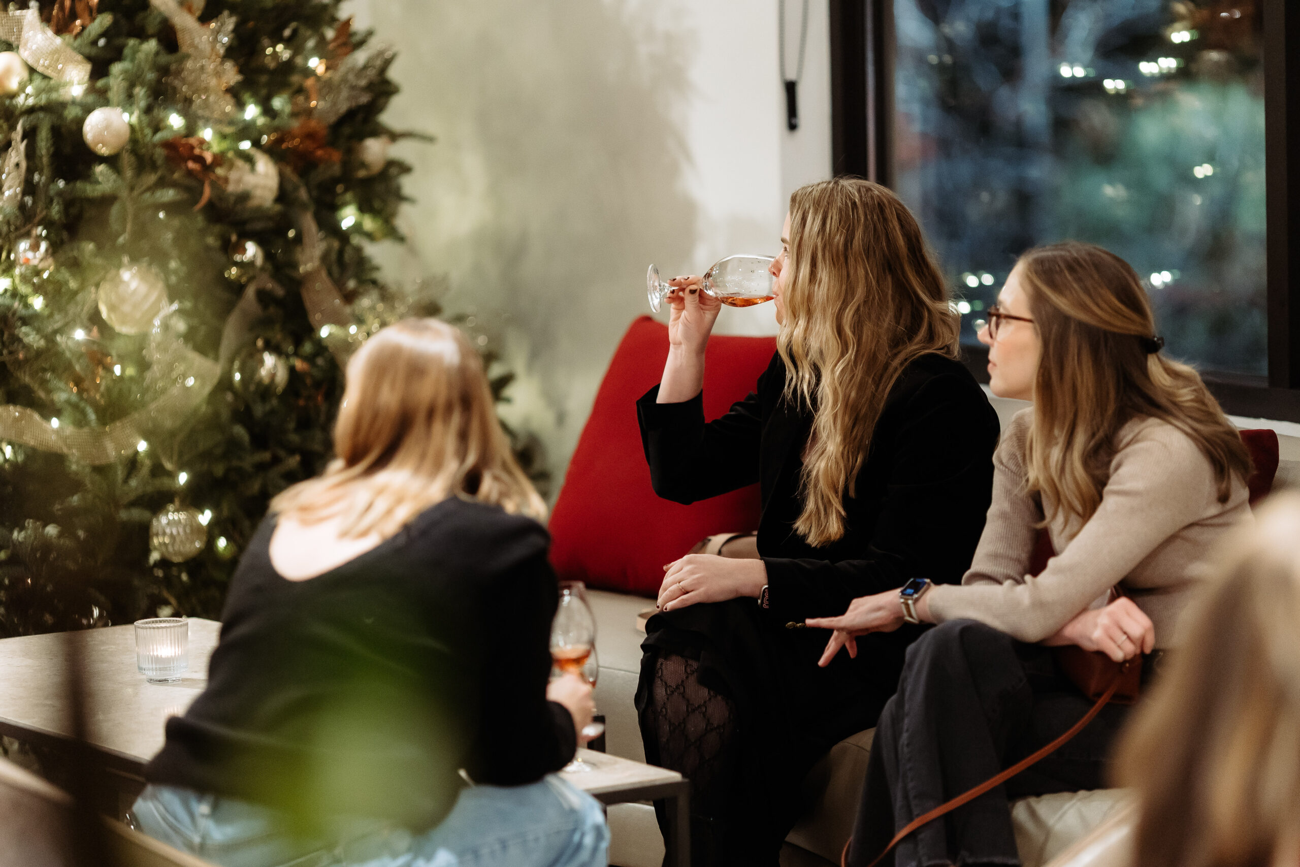 3 people sit in the lounge with glasses of wine gazing at a Christmas tree