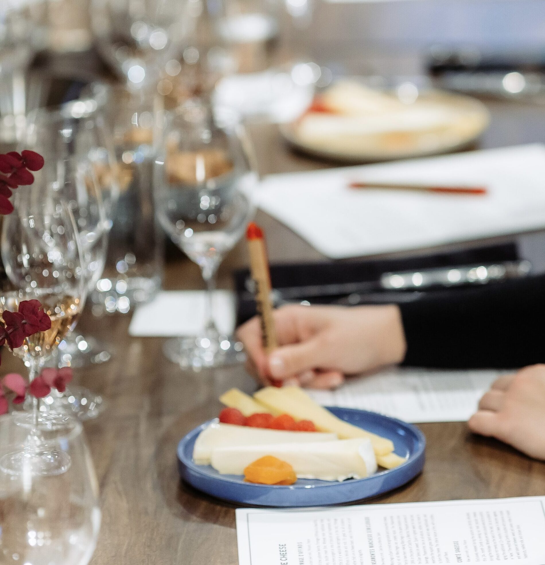 person takes notes at a wine class with a plate of cheese in front of them