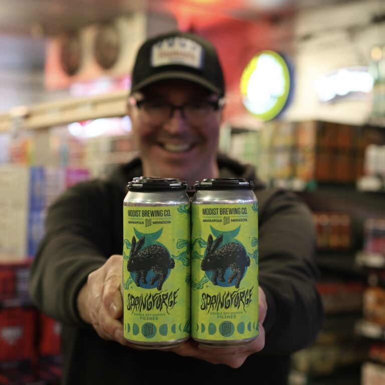 Bill holding up a 4 pack of Modist Springforge Double Dry Hopped Pilsner in the beer cooler