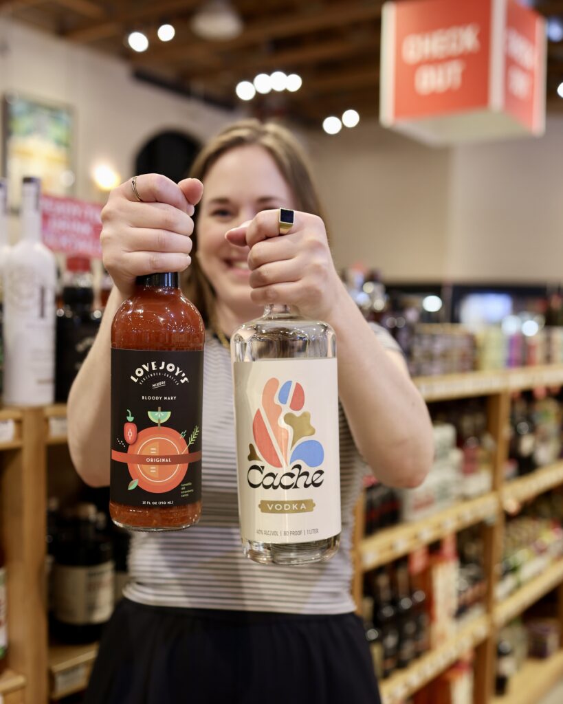 Sara holding up a bottle of Lovejoy Bloody Mary Mix and a bottle of Vodka