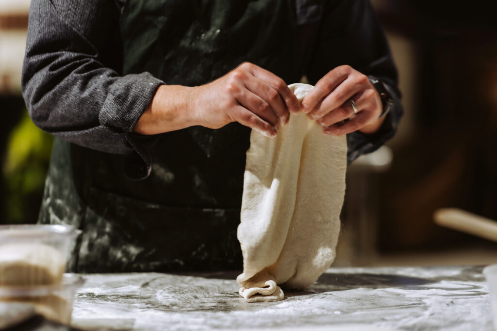 two hands stretch out a pizza dough