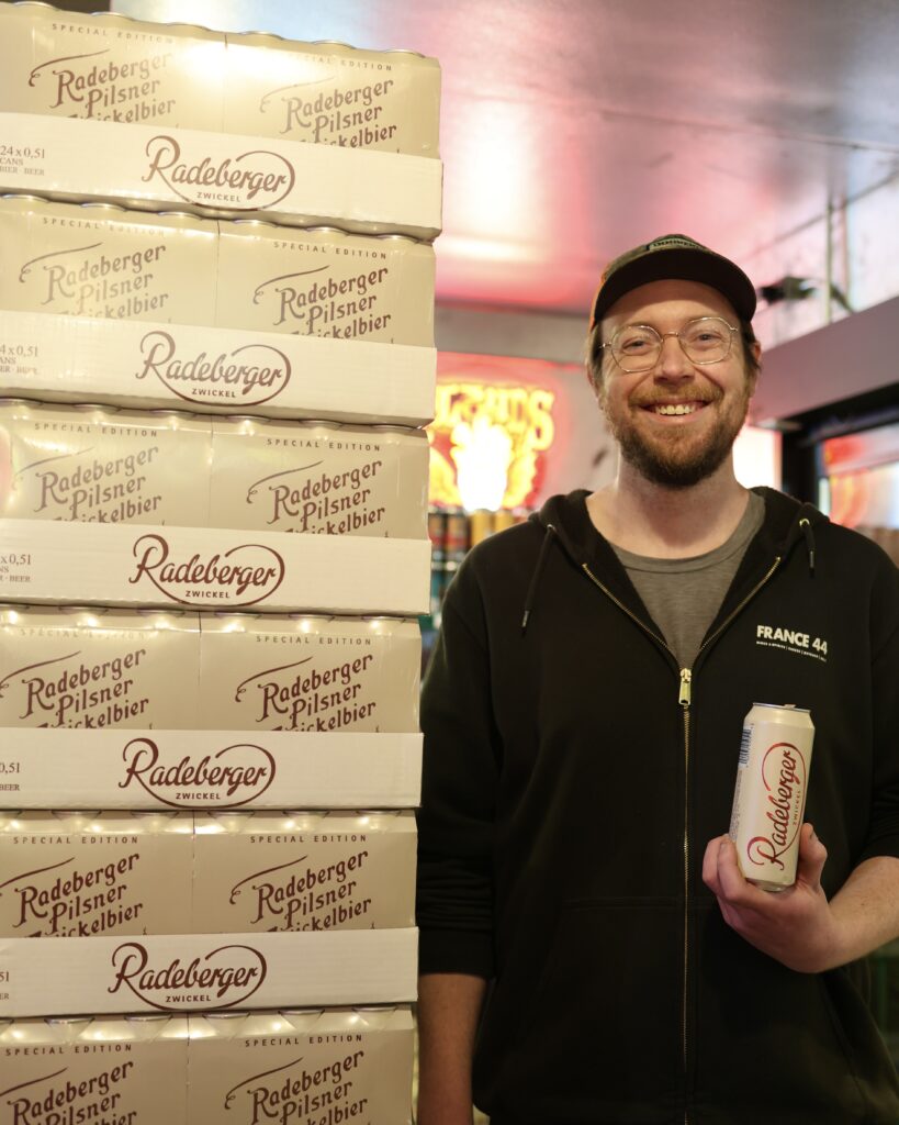 Stephen standing next to a stack of Radeberger Zwickelbier Pilsner while holding a can
