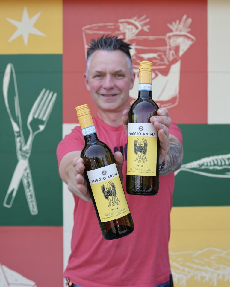 Troy holding two bottles of wine in front of a colorful mural