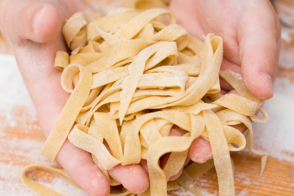 Hands holding fresh pasta over a floury board