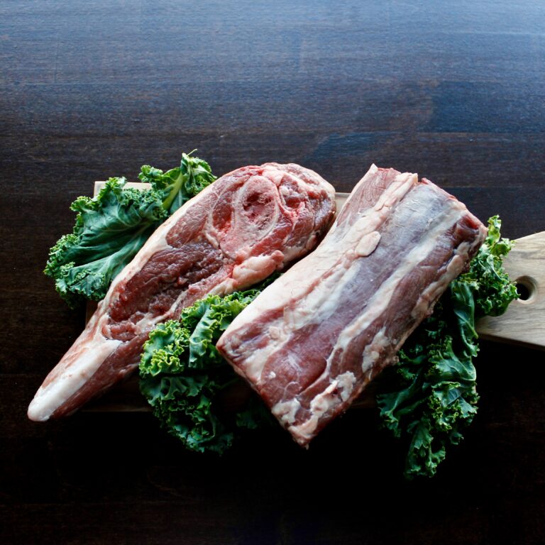 Lamb roasts on a wooden board surrounded by greenery and herbs