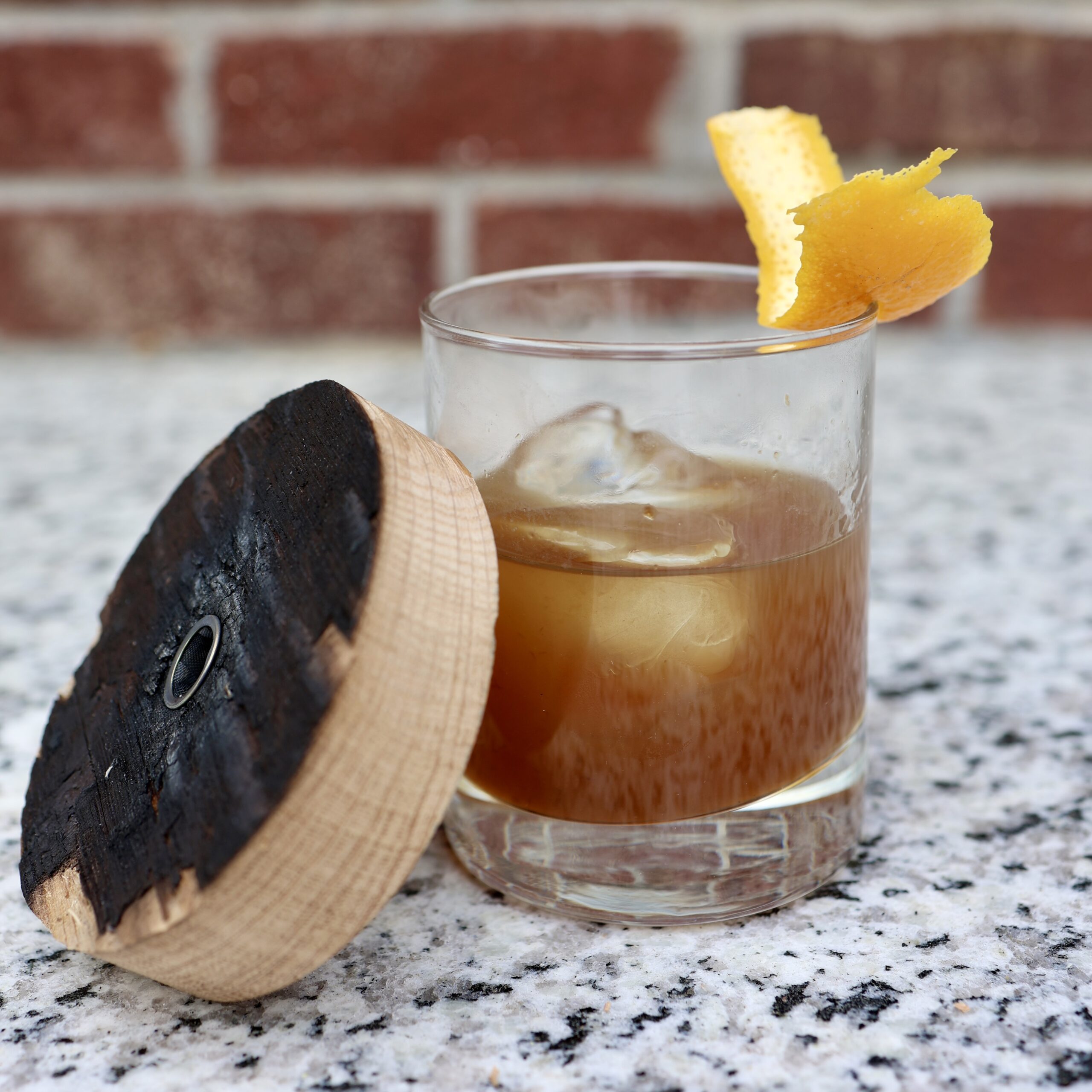 Cocktail smoker leaning against an old fashioned on a granite countertop
