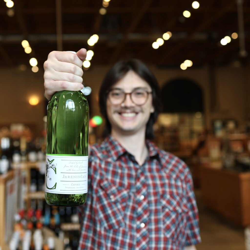 Joey holding up a green bottle of wine in the Liquor Store