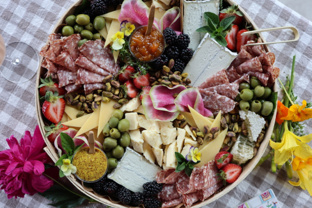 Colorful cheese & charcuterie board on a gingham table cloth beside a bottle of rosé