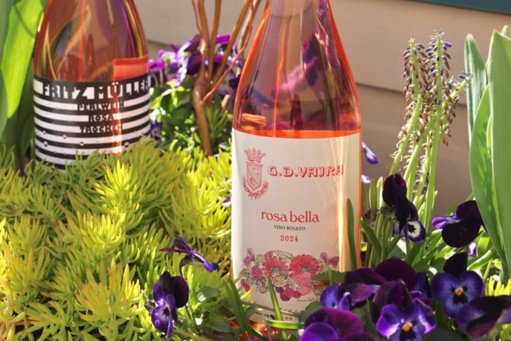 2 bottles of rosé sitting in a flower bed filled with purple pansies and greenery
