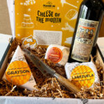Box filled with crinkle, a bottle of wine, three cheeses, and a cheese knife