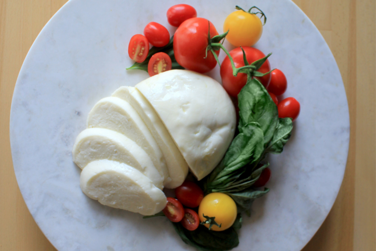 Mozzarella sliced on a marble plate with tomatoes and basil