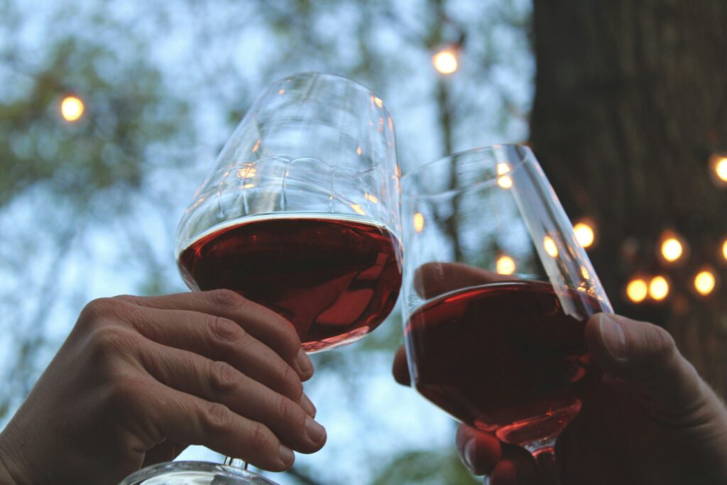 Two hands clinking red wine glasses in a yard