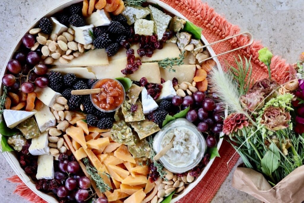 Round cheeseboard on an orange placemat next to a bouquet of flowers