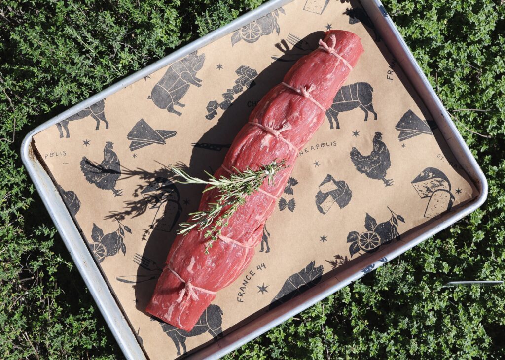 tied up beef tenderloin sitting on a sheet tray on a bed of thyme