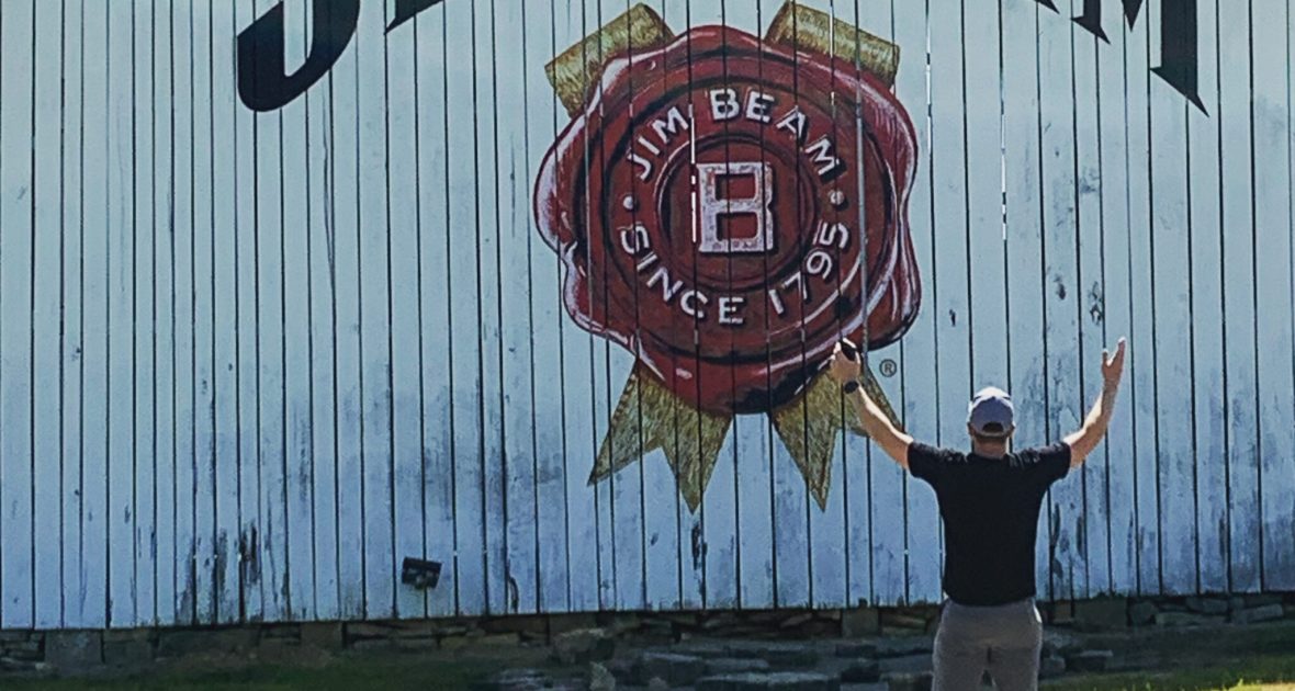Man poses in front of white barn with Jim Beam logo