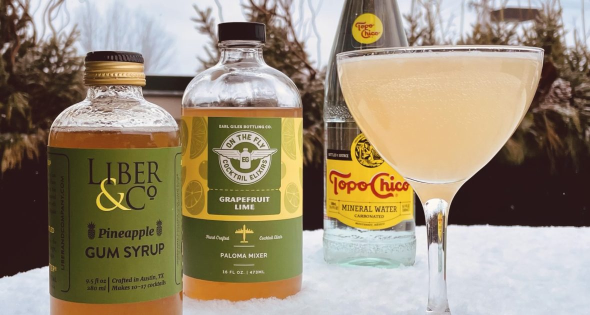 Cocktail in a coupe glass sits on a snowy table in front of three bottles